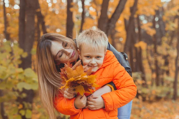 Moeder knuffelt haar kind tijdens een wandeling in het herfstpark. Herfstseizoen en eenouderconcept. — Stockfoto