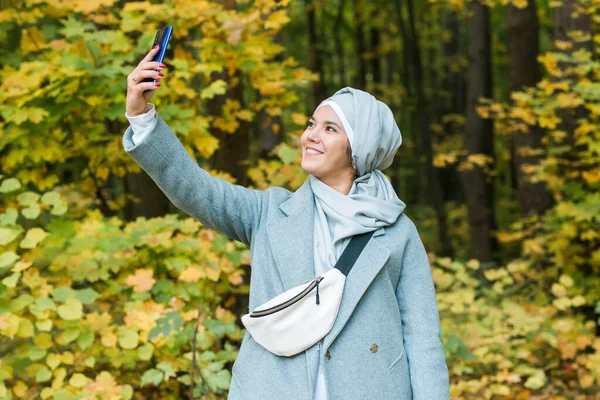 Jovem mulher muçulmana árabe em roupas hijab fazendo selfie tiro no celular no parque. Pessoas conceito de estilo de vida religioso. Espaço de cópia. — Fotografia de Stock
