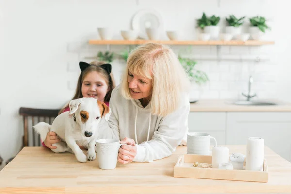 Bonne petite-fille et grand-mère dans la cuisine avec Jack Russell terrier chien. Grand-mère et petit-enfant passent du temps ensemble à la maison. Personnes âgées, concept de famille et de génération. — Photo