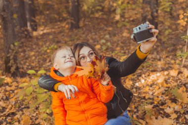 Oğlu ve annesi sonbahar parkında selfie çekiyorlar. Bekar ebeveyn, boş zaman ve sonbahar konsepti.