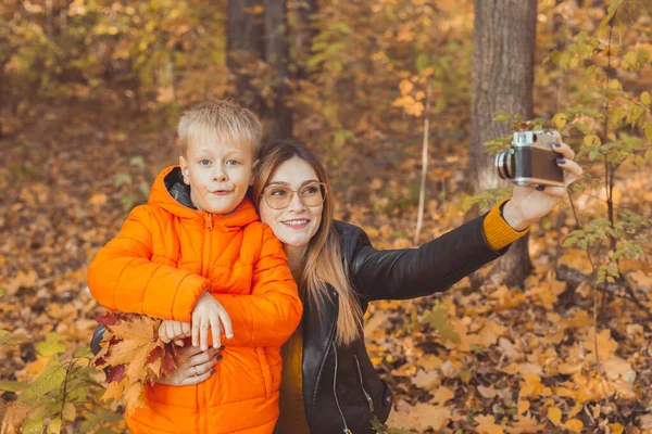 Hijo y madre se están tomando selfie en cámara en el parque de otoño. Concepto de temporada monoparental, de ocio y otoño. —  Fotos de Stock