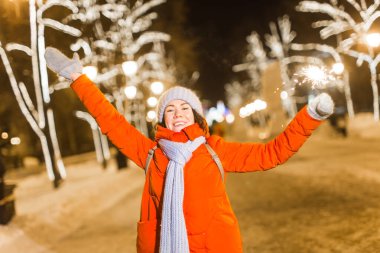 Elinde maytap tutan bir kız. Açık hava kış şehri arka planı, kar, kar taneleri.