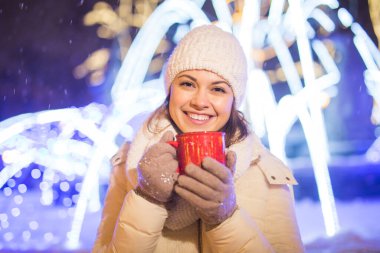 Kış boyunca ayakta duran kız. Arka planda kar yağıyordu. Sıcak ceket şapkası takıyor, çay ve sıcak çay içiyordu..