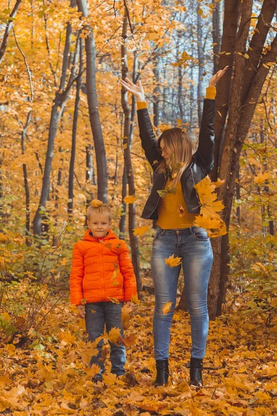 Bekar ebeveynler sonbahar yapraklarıyla parkta oynuyorlar. Mutlu anne ve oğul sonbahar yapraklarını sonbahar parkına atıyorlar.. — Stok fotoğraf