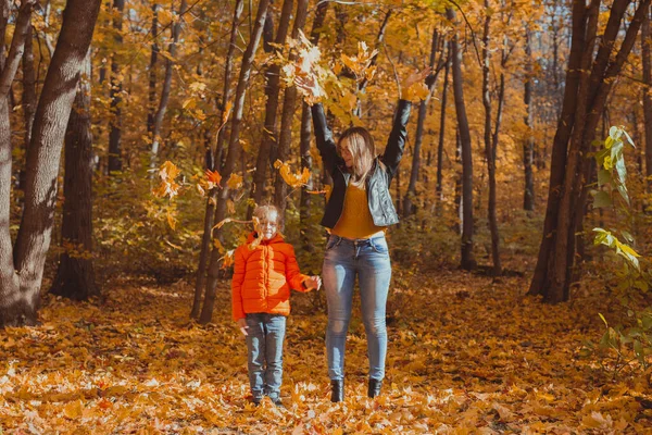 Bekar ebeveynler sonbahar yapraklarıyla parkta oynuyorlar. Mutlu anne ve oğul sonbahar yapraklarını sonbahar parkına atıyorlar.. — Stok fotoğraf