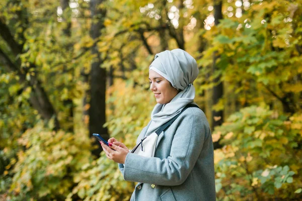 Dışarıda cep telefonu kullanan güzel bir müslüman kadın. Akıllı telefon kullanan Arap bir kadın tesettür takıyor. İslami kız şehir parkında mesaj atıyor. Boşluğu kopyala — Stok fotoğraf