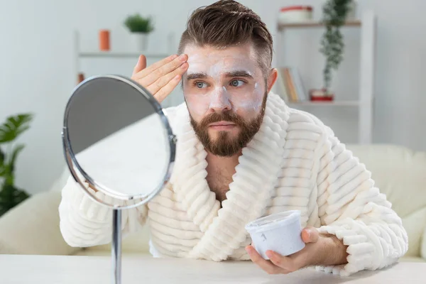 Бородатий хлопець наносить крем для обличчя перед дзеркалом Догляд за шкірою та спа для концепції людини . — стокове фото