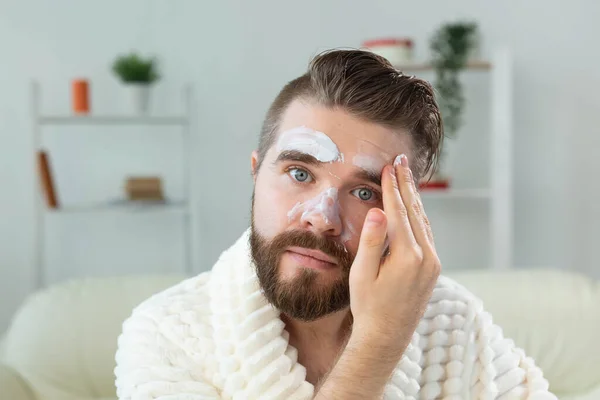 Бородатий хлопець наносить крем проти зморшок на обличчя. Догляд за шкірою та спа для людини концепція . — стокове фото
