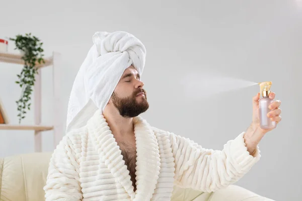 Бородатый самец с полотенцем на голове, нанося на лицо обработку брызгающей воды. Спа, уход за телом и кожей для человека. — стоковое фото