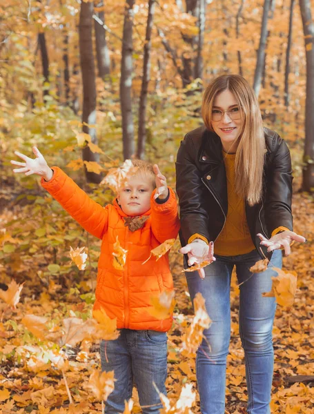 Bekar ebeveynler sonbahar yapraklarıyla parkta oynuyorlar. Mutlu anne ve oğul sonbahar yapraklarını sonbahar parkına atıyorlar.. — Stok fotoğraf