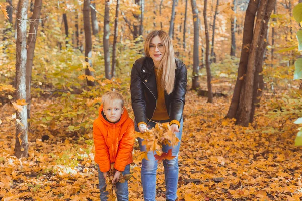 Bekar ebeveynler sonbahar yapraklarıyla parkta oynuyorlar. Mutlu anne ve oğul sonbahar yapraklarını sonbahar parkına atıyorlar.. — Stok fotoğraf