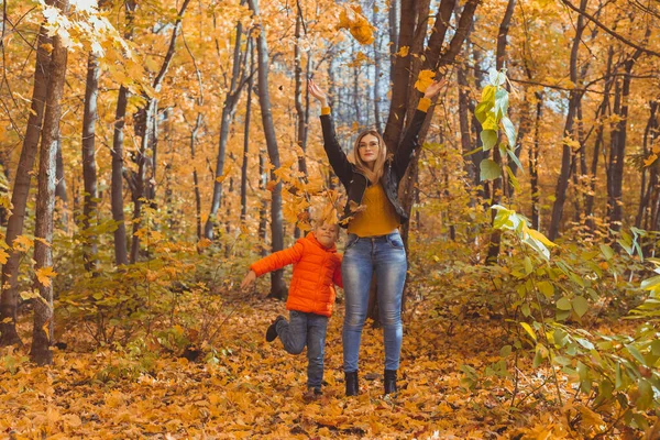 Rodzina samotnych rodziców bawiąca się jesiennymi liśćmi w parku. szczęśliwy Mama i syn rzucać jesienią liście w górę w jesienny park. — Zdjęcie stockowe