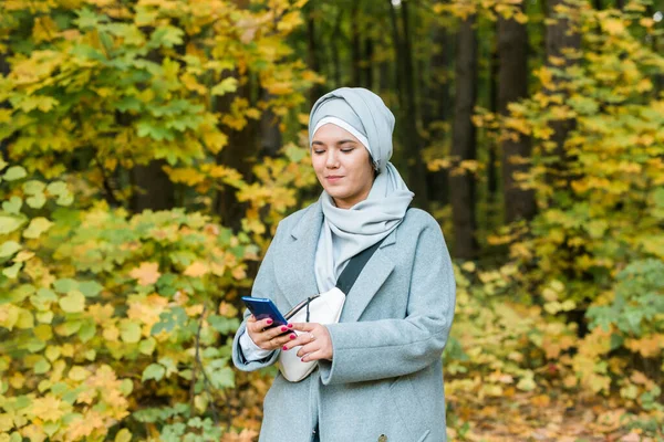 Mulher muçulmana no parque usando smartphone conectado on-line sem fio. Espaço para propaganda — Fotografia de Stock