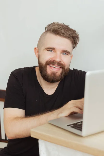 Feliz joven sonriente mirando y trabajando en la computadora portátil en casa. Tecnologías, trabajo remoto y redes sociales — Foto de Stock
