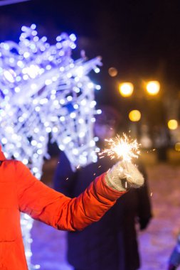 Örgü şapkalı ve atkılı kadın Bengal ışığı ve maytapla şehirde dikiliyor. Kutlama ve Noel kavramı.