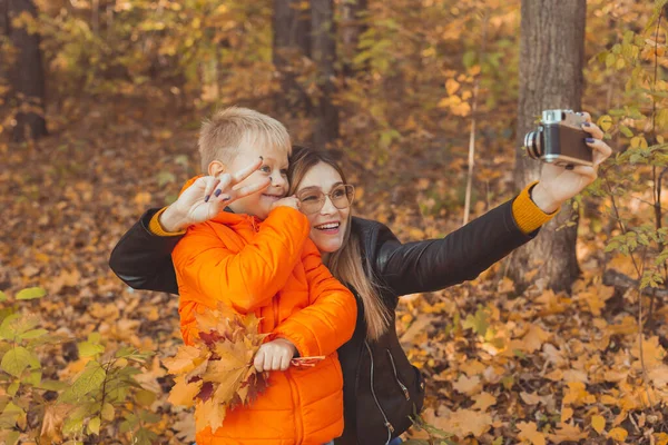 Hijo y madre se están tomando selfie en cámara en el parque de otoño. Concepto de temporada monoparental, de ocio y otoño. — Foto de Stock