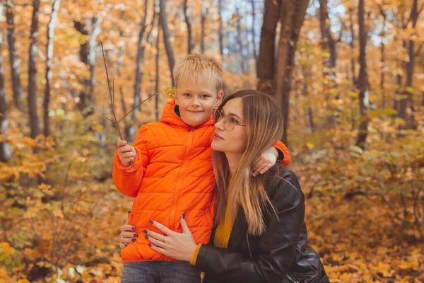 妈妈在秋天的公园散步时拥抱她的孩子.秋季和单亲家庭的概念. — 图库照片