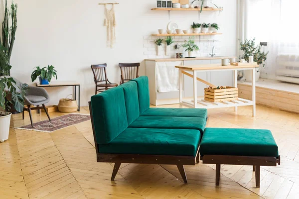 Stylový interiér domu se zelenou pohovkou a skandinávskou kuchyní na pozadí. Hnědá dřevěná podlaha — Stock fotografie
