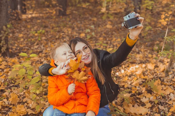 儿子和母亲正在秋天公园的摄像机前自拍。单亲、闲暇和秋天的概念. — 图库照片