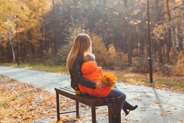 Madre soltera y niño en el otoño en el parque se sientan en el banco. Temporada de otoño y concepto familiar. —  Fotos de Stock