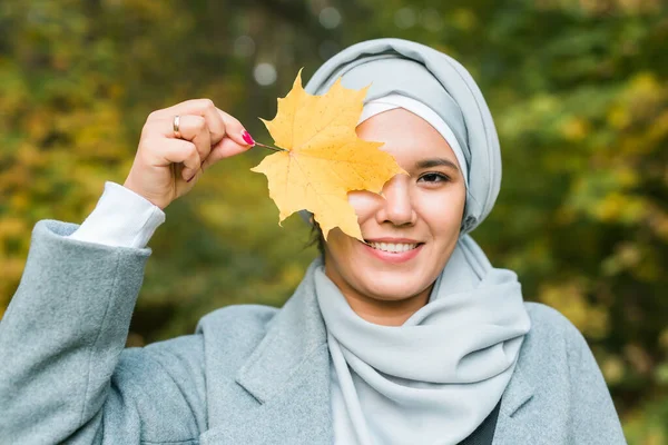 Sonbahar Müslüman kadın güneşli bir günde dışarıda akçaağaç yaprağı tutuyor. Sonbahar parkında tesettürlü güzel bir Arap kız. — Stok fotoğraf