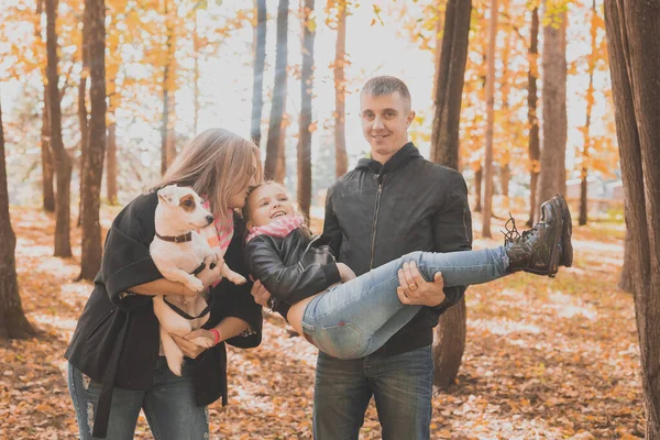 La famiglia passa il tempo in parco di autunno con un cane. Padre, madre e figlia e Jack Russell terrier cane divertirsi in autunno — Foto Stock