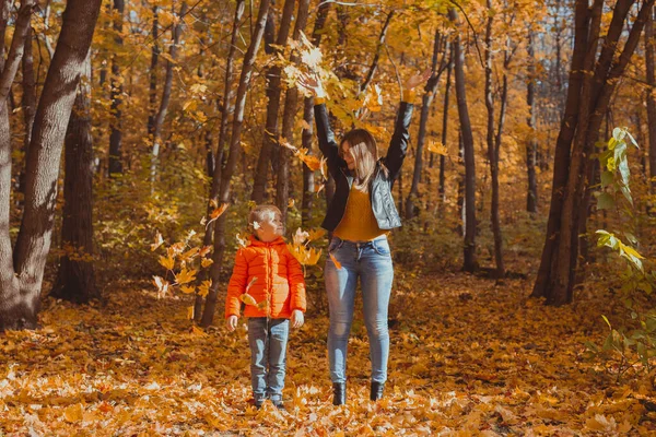 Bekar ebeveynler sonbahar yapraklarıyla parkta oynuyorlar. Mutlu anne ve oğul sonbahar yapraklarını sonbahar parkına atıyorlar.. — Stok fotoğraf