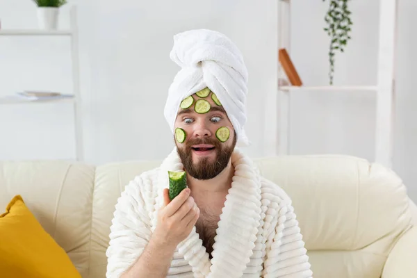 Homme barbu drôle tenant des tranches de concombre sur le visage. Spa à la maison, soins du corps et de la peau pour le concept masculin. — Photo