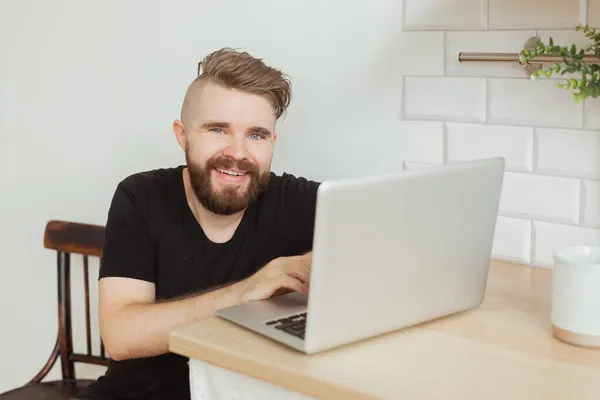 Feliz joven sonriente mirando y trabajando en la computadora portátil en casa. Tecnologías, trabajo remoto y redes sociales — Foto de Stock