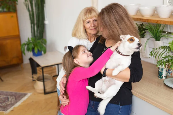 Bonne petite-fille et grand-mère et fille s'amuser avec Jack Russell terrier chien. Grand-mère embrasse son petit-enfant à la maison. Relation, famille et concept de trois générations. — Photo