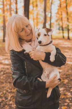 Sonbahar parkında köpeğini kucaklayan kıdemli bir kadın. Etkin yaşlanma ve evcil hayvan konsepti.