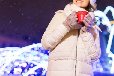 Kış boyunca ayakta duran kız. Arka planda kar yağıyordu. Sıcak ceket şapkası takıyor, çay ve sıcak çay içiyordu..