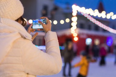 Pistte bir kadın kayıyor ve akıllı telefondan fotoğraf çekiyor. Yeni yıl arifesi ve Noel. Peri ışıkları. Buz ve kar ruh hali konsepti. Kış sporu.