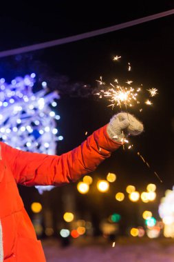 Kış örgü giysileri giyen, kar zemini üzerinde maytap tutan yakın plan bir kadın. Noel tatili.