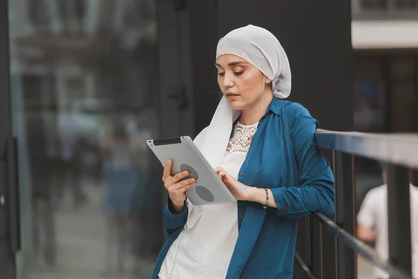 Retrato de uma estudante árabe segurando um tablet. Mulher de negócios árabe em hijab segurando um tablet na rua. Mulher está vestida com hijab — Fotografia de Stock