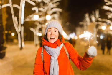 Elinde maytap tutan bir kız. Açık hava kış şehri arka planı, kar, kar taneleri.