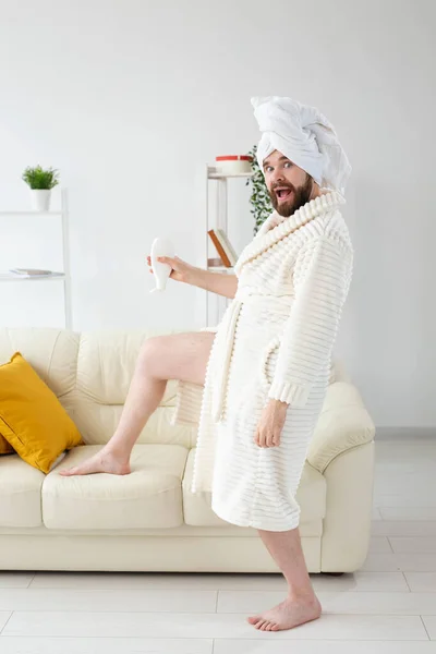 Забавный портрет красивого парня в полотенце и халате с трубкой крема для тела в руке. Спа, уход за телом и кожей для человека — стоковое фото