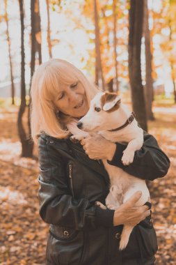 Sonbahar parkında köpeğini kucaklayan kıdemli bir kadın. Etkin yaşlanma ve evcil hayvan konsepti.