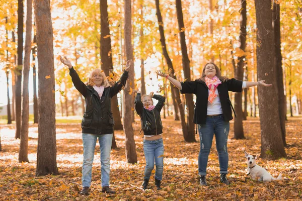 Großmutter und Mutter mit Enkelin werfen Herbstlaub in den Herbstpark und amüsieren sich. Generation, Freizeit und Familienkonzept. — Stockfoto