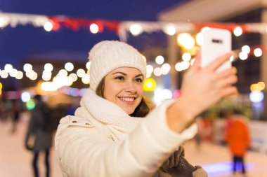 Kışın buz pistinde mutlu genç bir kadın akıllı telefondan fotoğraf çekiyor, selfie çekiyor..