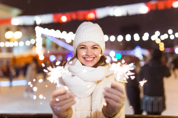 Örgü şapkalı ve atkılı genç bir kadın Bengal ışığı ve maytapla şehirde dikiliyor. Kutlama ve Noel kavramı.
