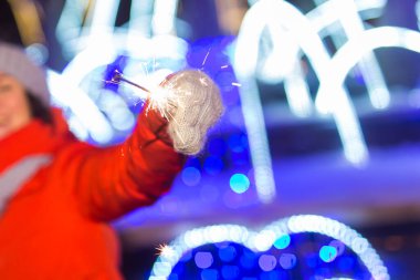 Örgü şapkalı ve atkılı kadın Bengal ışığı ve maytapla şehirde dikiliyor. Kutlama ve Noel kavramı.