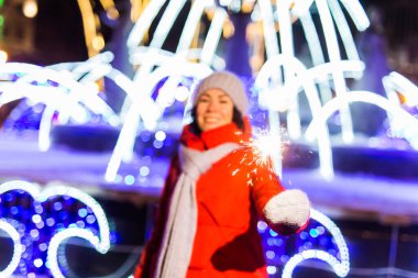 Örgü şapkalı ve fularlı genç bir kadın Bengal ışığı ve maytapla şehirde dikiliyor. Kutlama ve Noel kavramı.