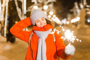 Elinde maytap tutan bir kız. Açık hava kış şehri arka planı, kar, kar taneleri.