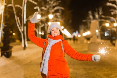 Örgü şapkalı ve atkılı genç bir kadın Bengal ışığı ve maytapla şehirde dikiliyor. Kutlama ve Noel kavramı.