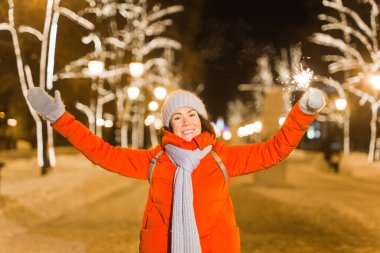 Elinde maytap tutan bir kız. Açık hava kış şehri arka planı, kar, kar taneleri.