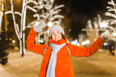 Elinde maytap tutan bir kız. Açık hava kış şehri arka planı, kar, kar taneleri.