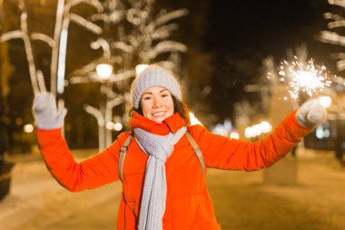 Elinde maytap tutan bir kız. Açık hava kış şehri arka planı, kar, kar taneleri.