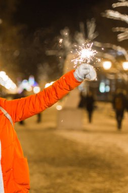 Örgü şapkalı ve atkılı genç bir kadın Bengal ışığı ve maytapla şehirde dikiliyor. Kutlama ve Noel kavramı.