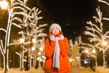 Kış tatili. Noel, yeni yıl konsepti. Komik mutlu kadın, şehrin sokaklarında aydınlanmış ve süslenmiş bir şekilde eğleniyor..